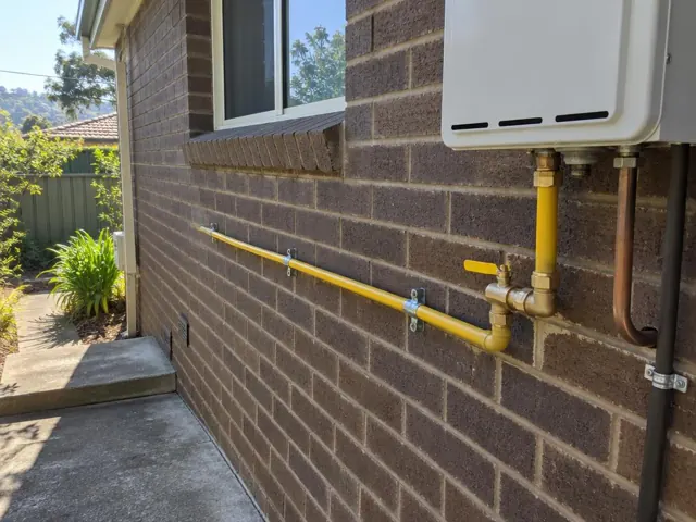 Yellow gas pipe and fittings on a brick exterior wall beside a hot water unit in Hornsby